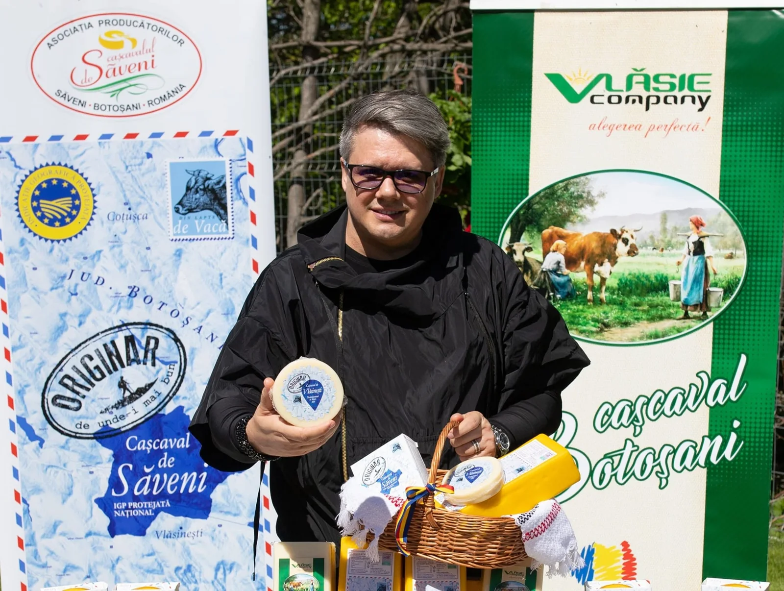 Fuego ținând un cașcaval și un coș cu produse Vlăsie, lângă bannerele Cașcaval de Săveni și Vlăsie Company